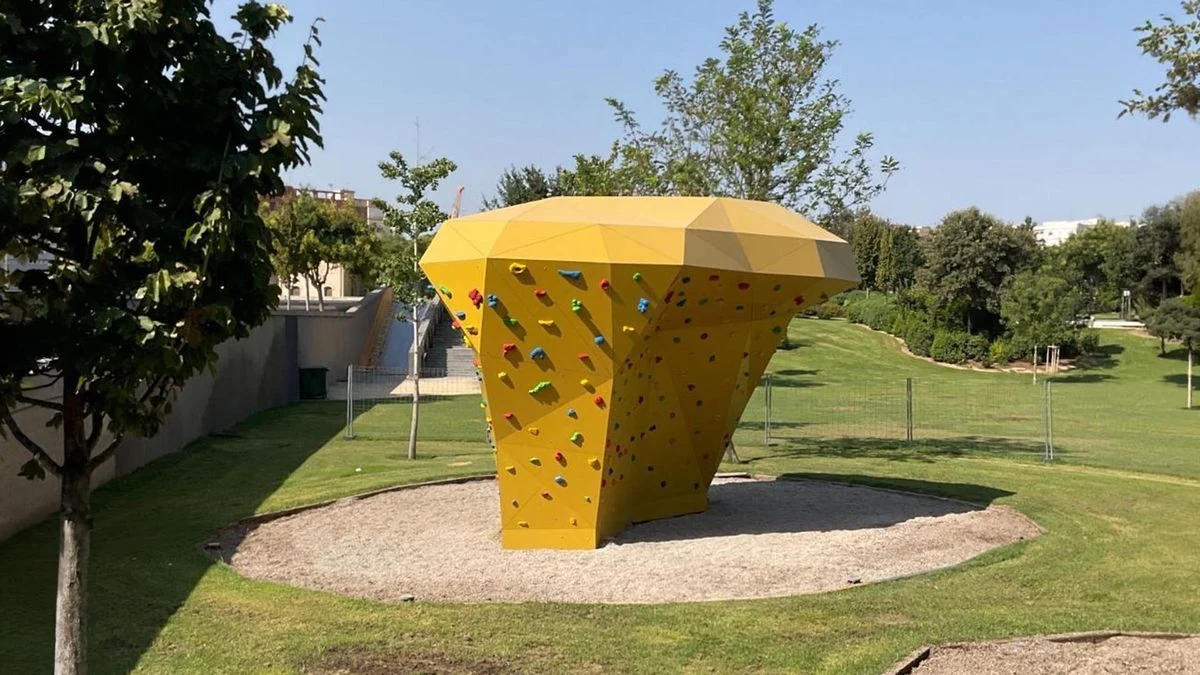 Imagen ilustrativa: un rocódromo al aire libre con presas de colores y una zona de seguridad, en un parque urbano con luz natural.