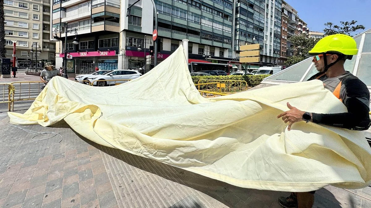 Imagen ilustrativa: lonas de sombra tensadas sobre una plaza urbana vacía, con luz solar filtrándose y edificios genéricos al fondo.