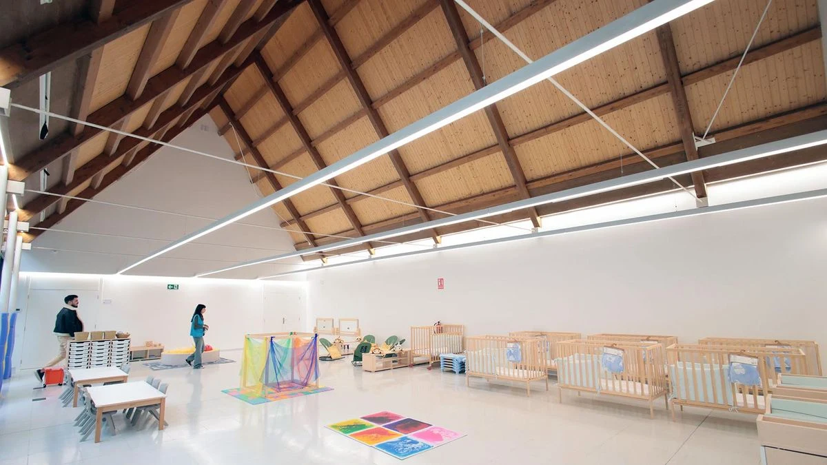 Imagen ilustrativa: fachada de un centro cívico moderno al atardecer, con una mano infantil tocando un ventanal