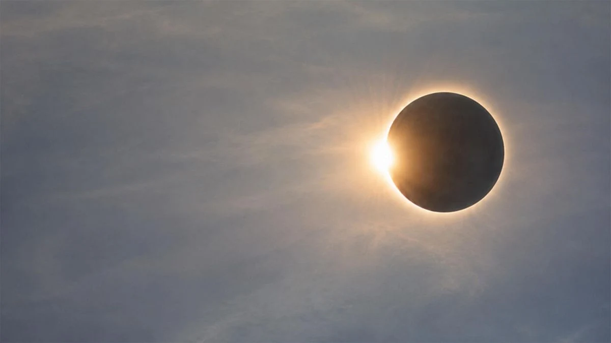 Imagen ilustrativa: vista de un paseo marítimo con personas mirando al cielo durante un eclipse parcial.