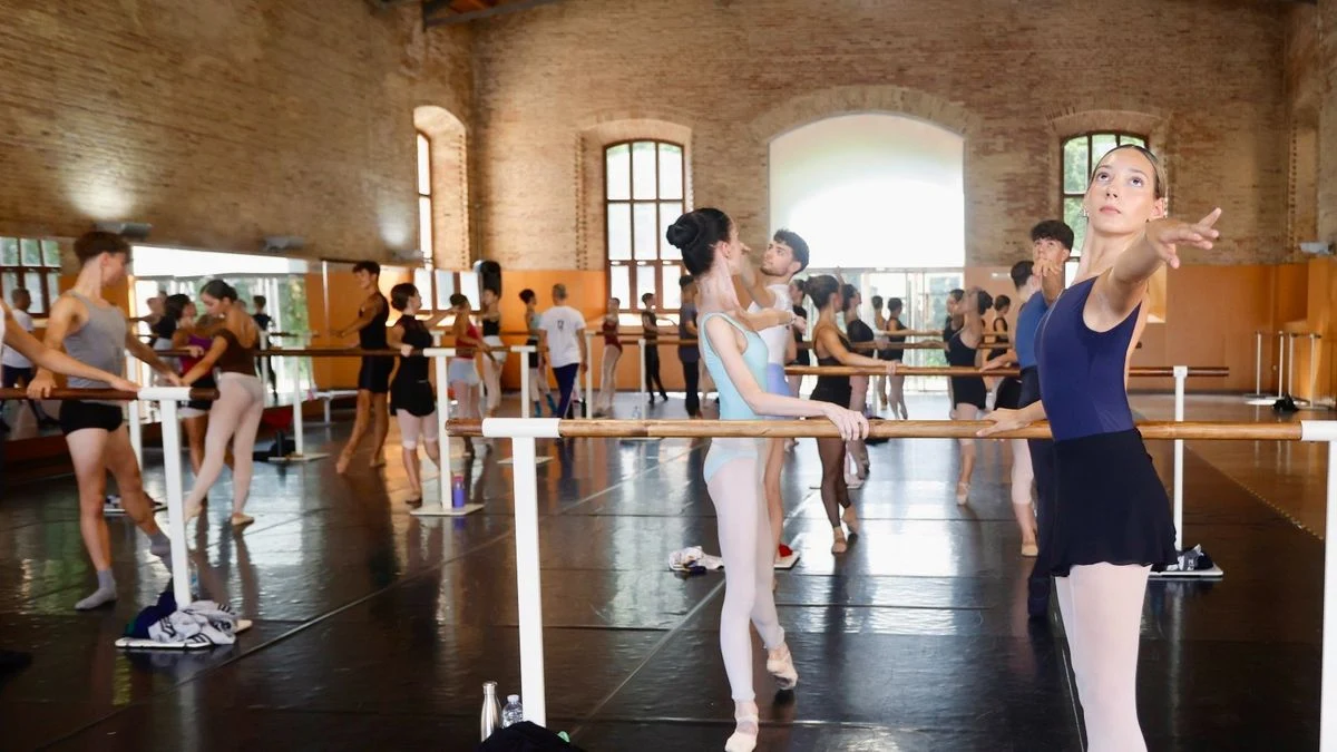 Imagen ilustrativa: un estudio de danza luminoso con barra y ventanales, con bailarines de fondo desenfocados