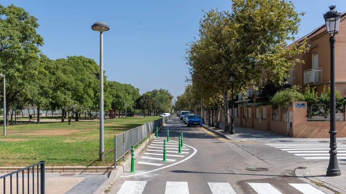Imagen ilustrativa: una intersección de un barrio residencial con una extensión de acera pintada y bolardos, junto a un paso de peatones y un parque.