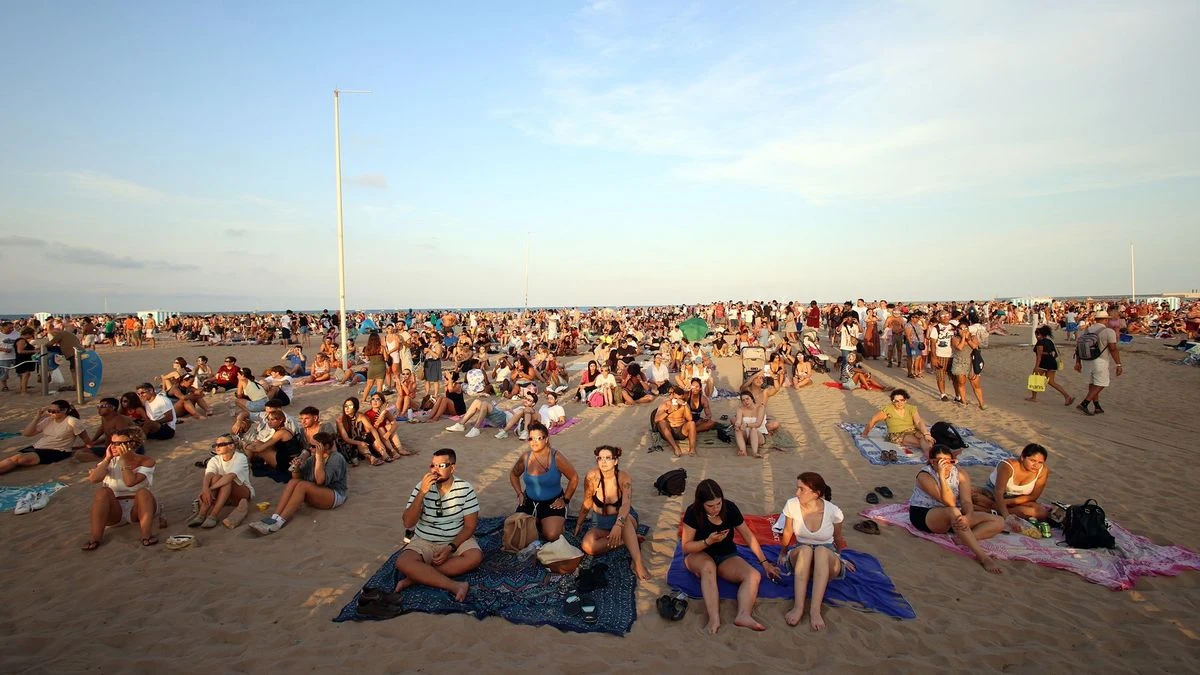 Imagen ilustrativa: playa amplia al anochecer con luz artificial de farolas y algunas personas como siluetas lejanas