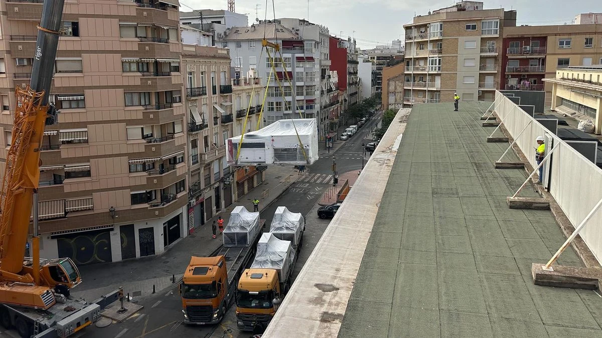 Imagen ilustrativa: grúa colocando equipos de aire acondicionado en la cubierta de un mercado municipal, con la calle al fondo.