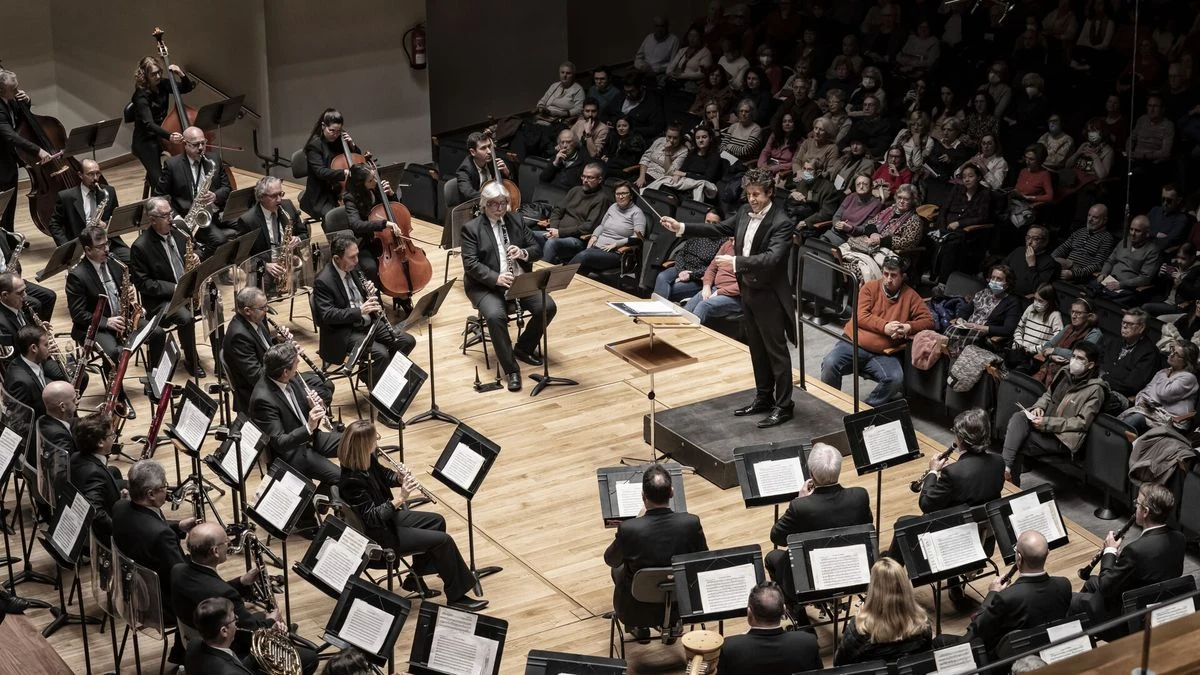Imagen ilustrativa: una partitura y una batuta sobre un atril de música en un escenario vacío