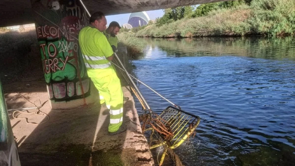 Imagen ilustrativa: el viejo cauce del Turia con un puente y residuos acumulados en el agua, con un operario de espaldas trabajando en la limpieza.
