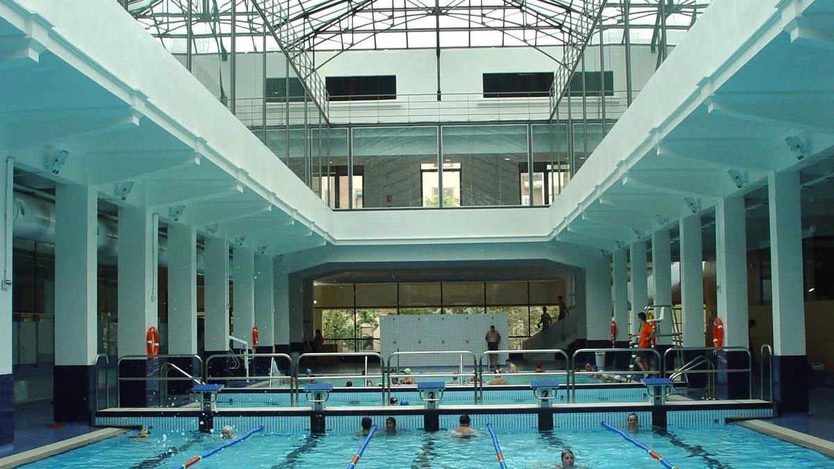 Imagen ilustrativa: interior de un complejo deportivo en obras, con piscina cubierta y material de construcción.