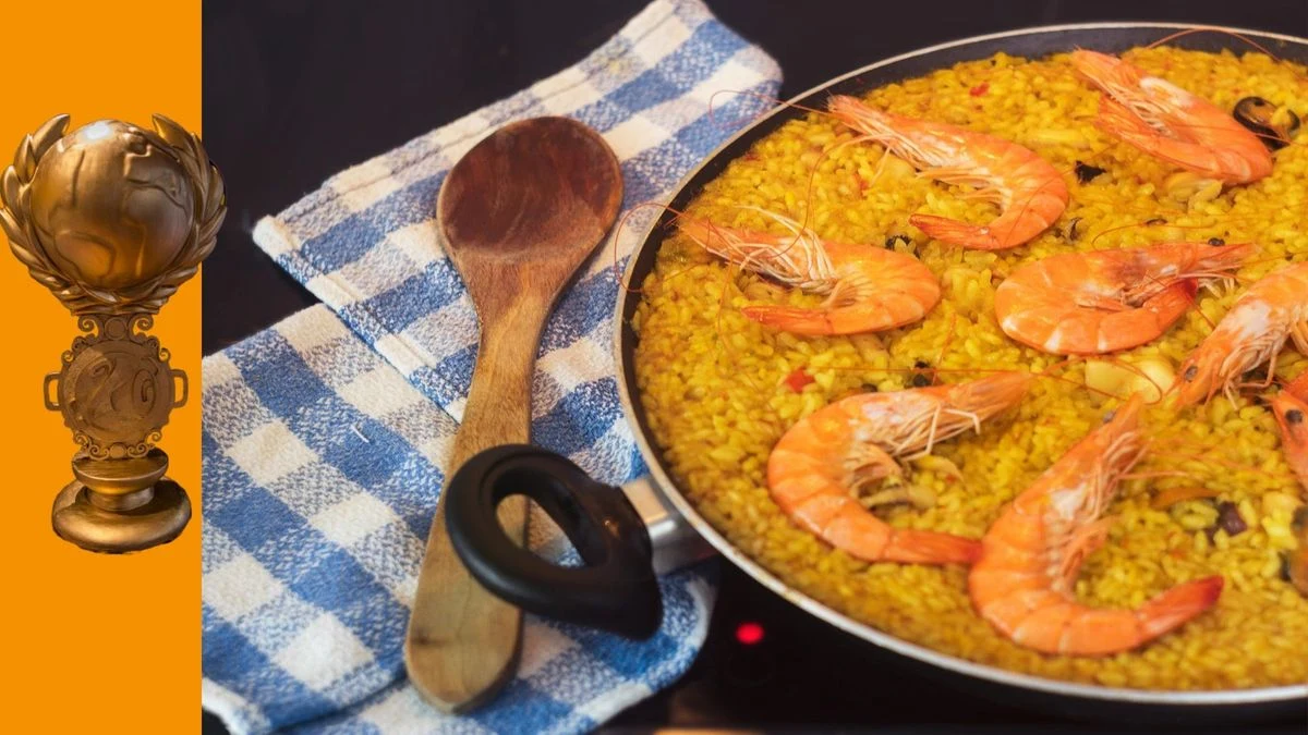 Imagen ilustrativa: una paella valenciana tradicional en una paellera sobre una mesa de madera al aire libre, con un fondo de puerto deportivo mediterráneo.