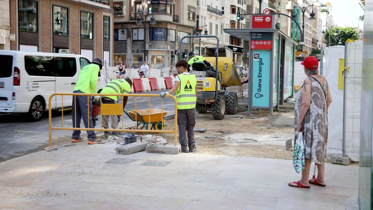 Imagen ilustrativa: acera en obras con adoquines de granito y un operario de espaldas trabajando, en una calle comercial.